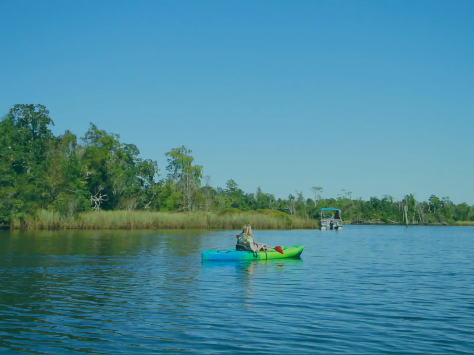 A kayaker and a pontoon boat on the bayou at Swamp House